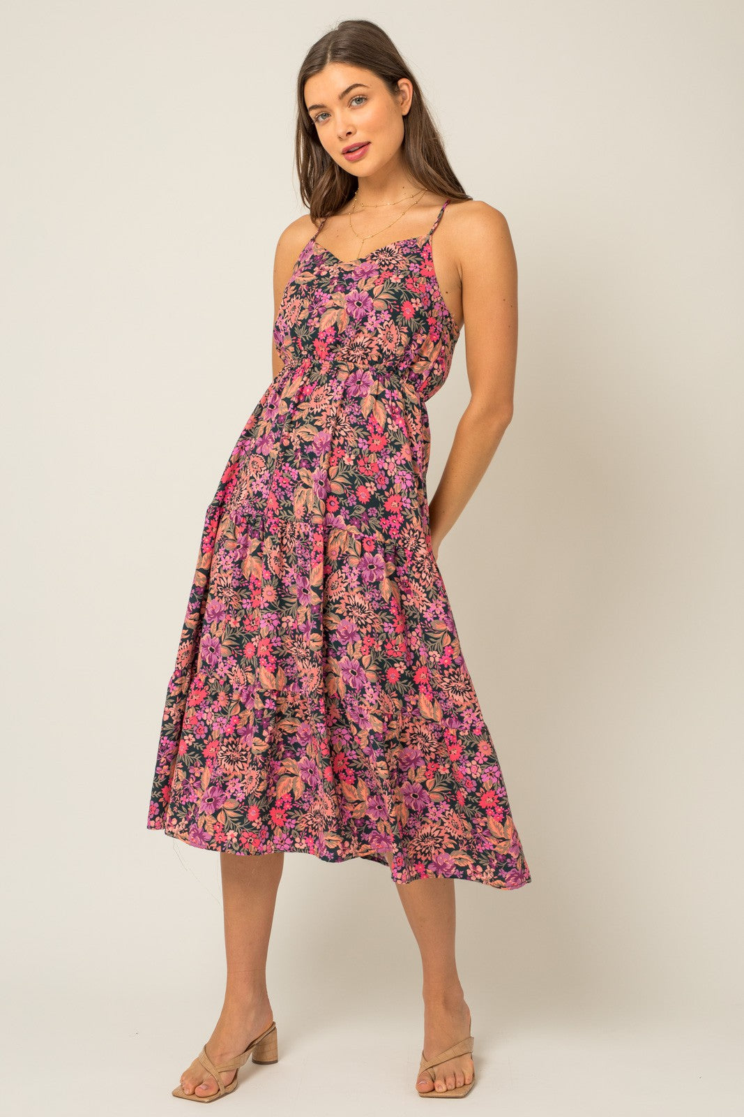 woman wearing a floral print midi dress with spaghetti straps and a flared skirt in vibrant pink and purple tones
