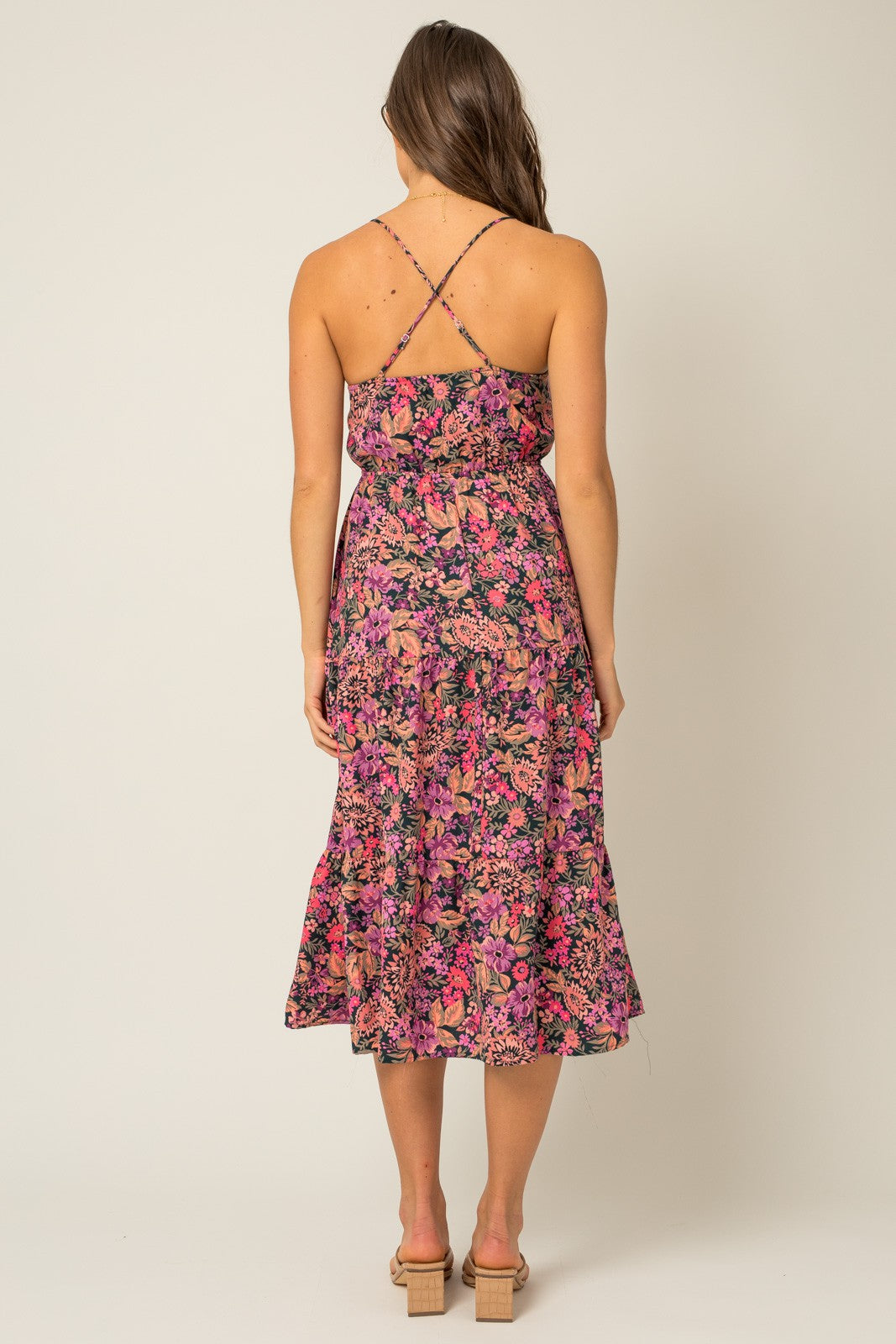 woman wearing a sleeveless floral maxi dress with a crisscross back design and a flared hemline