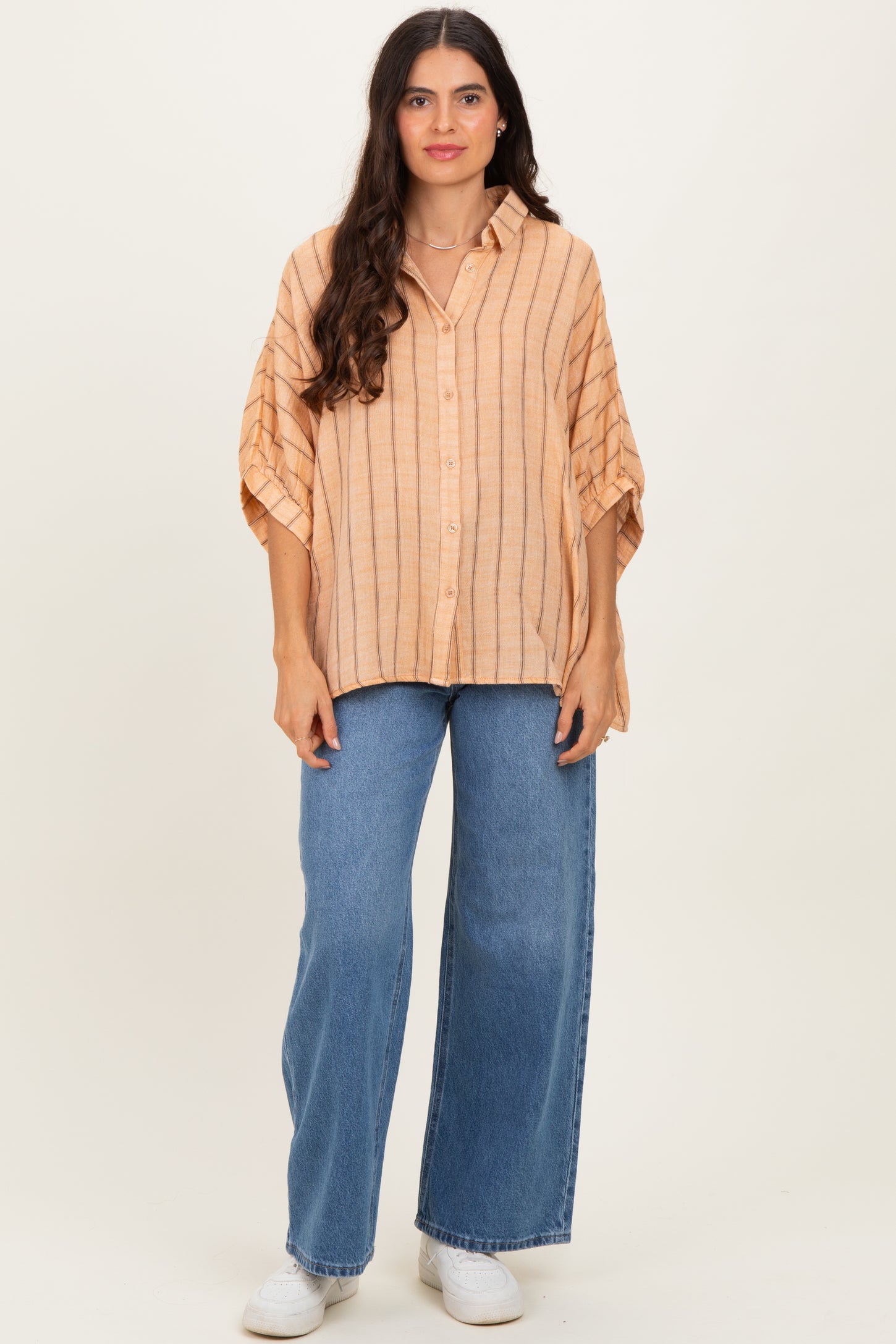 woman wearing a light orange striped oversized button-up shirt with wide sleeves and blue high-waisted jeans