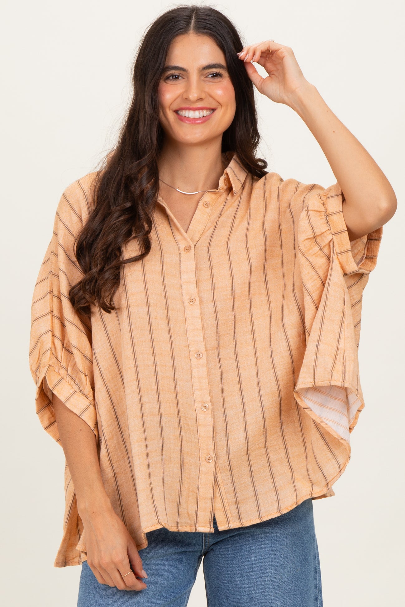 woman wearing a light orange striped oversized button-up shirt with short sleeves and a relaxed fit