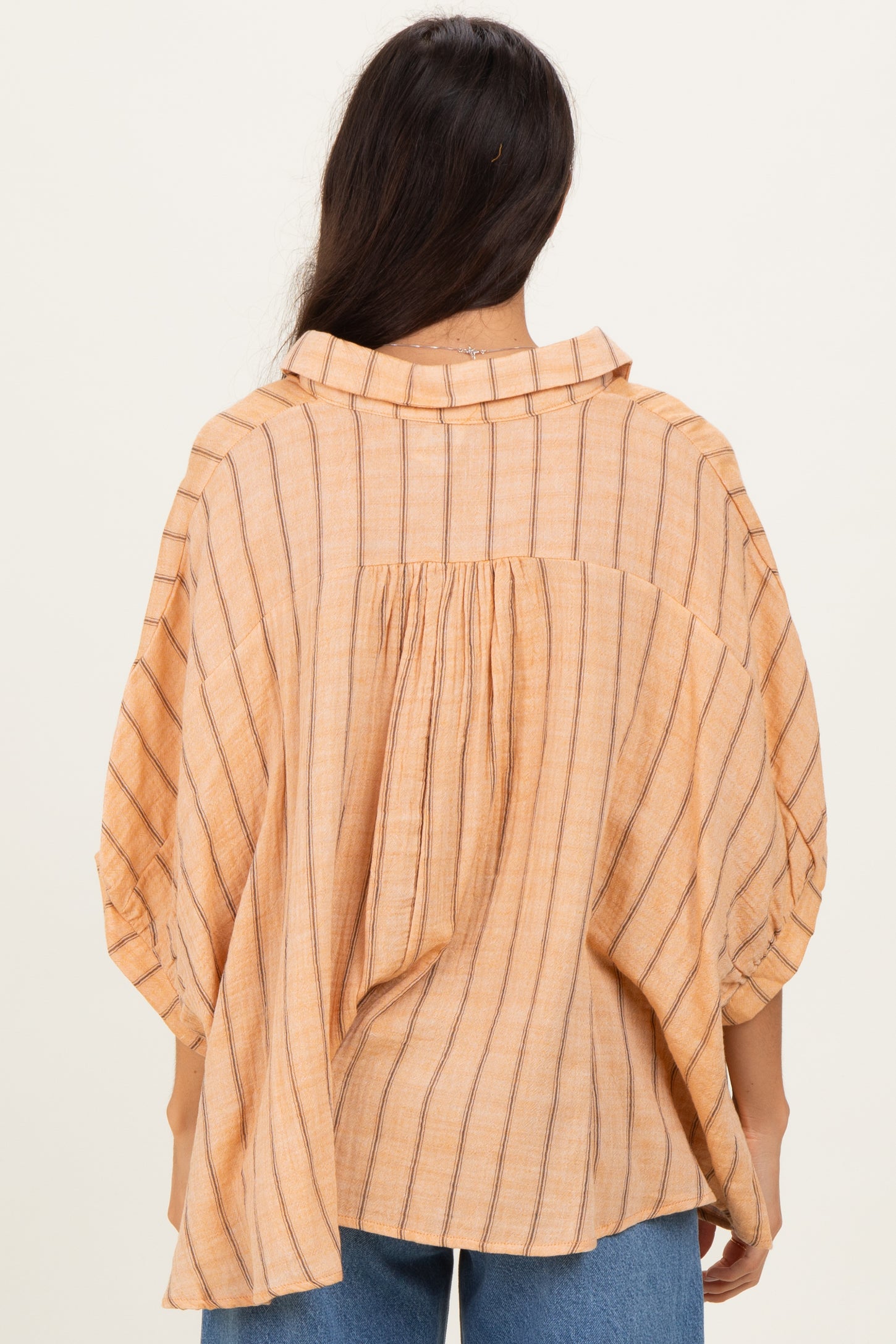 woman wearing a peach striped oversized blouse with a buttoned collar and gathered back detail