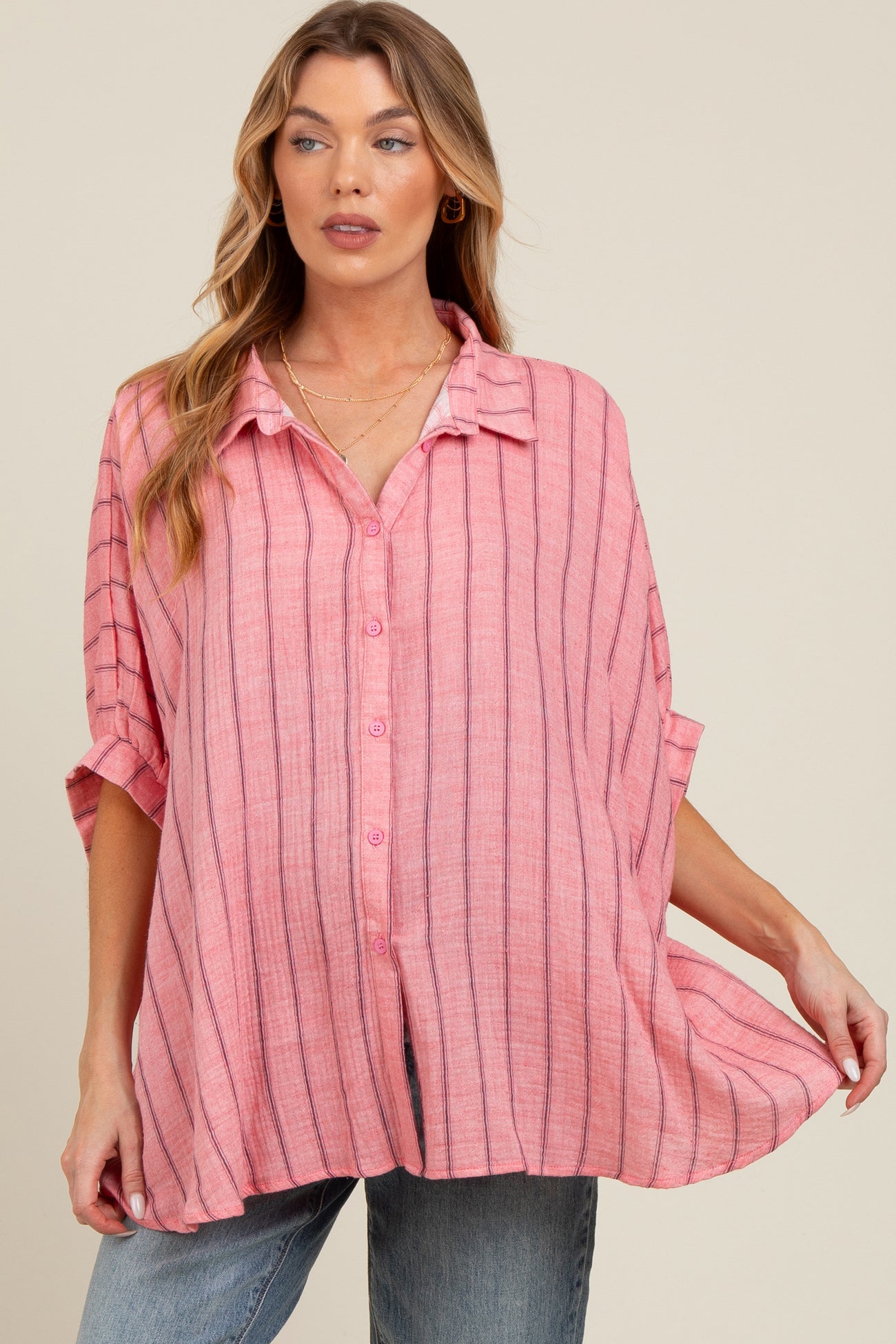 woman wearing a pink striped maternity button-up shirt, styled with rolled sleeves and a relaxed fit, showcasing her baby bump