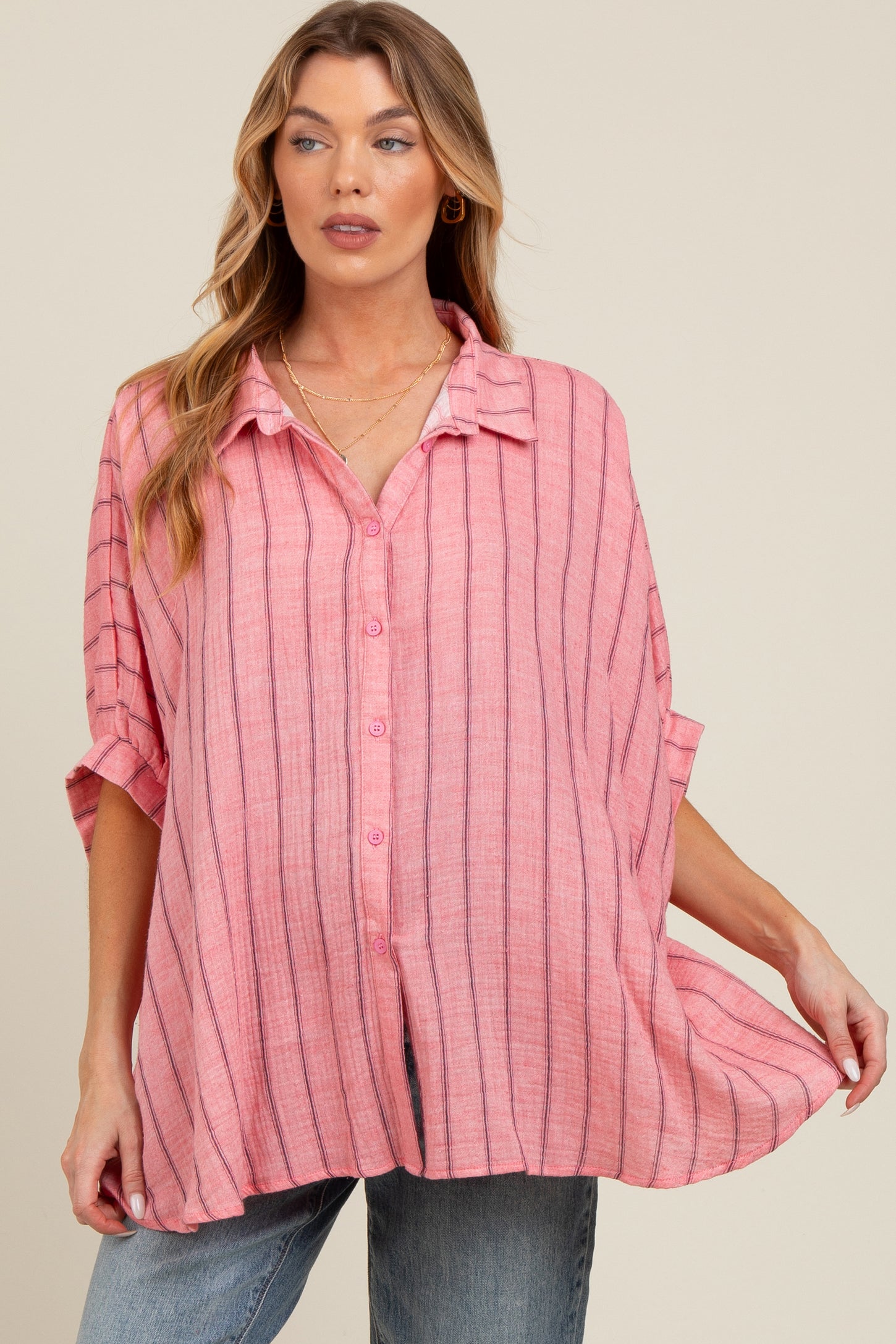 woman wearing a pink striped maternity button-up shirt, styled with rolled sleeves and a relaxed fit, showcasing her baby bump