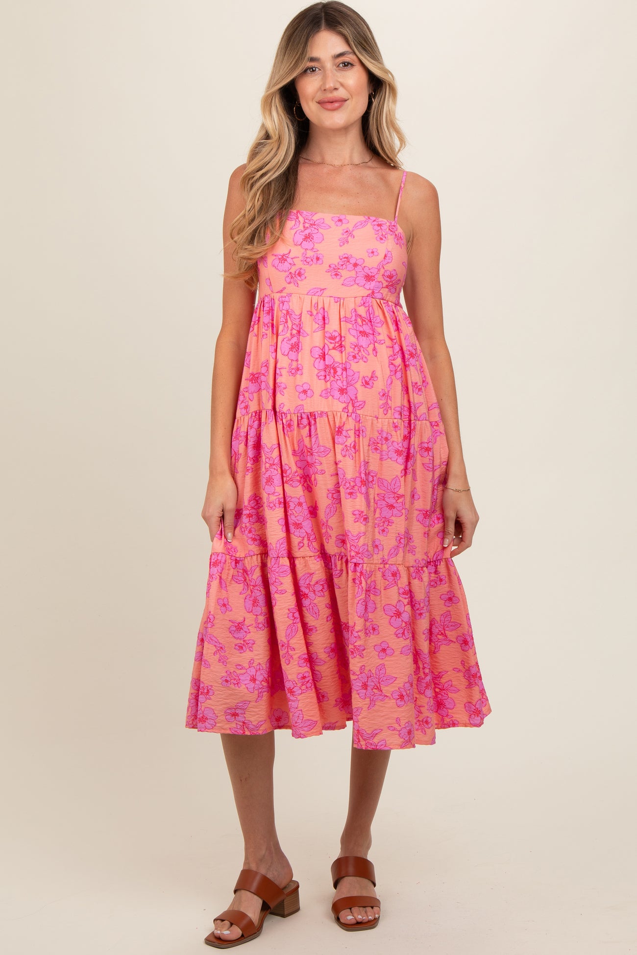 woman wearing a pink floral maternity dress with spaghetti straps and a tiered skirt