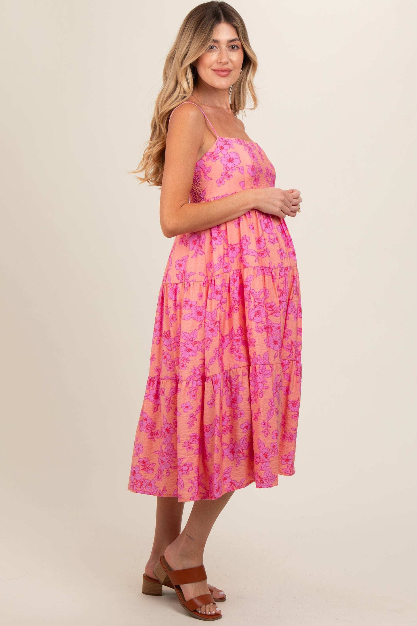 woman wearing a pink floral maternity dress with a tiered design and spaghetti straps, showing her baby bump