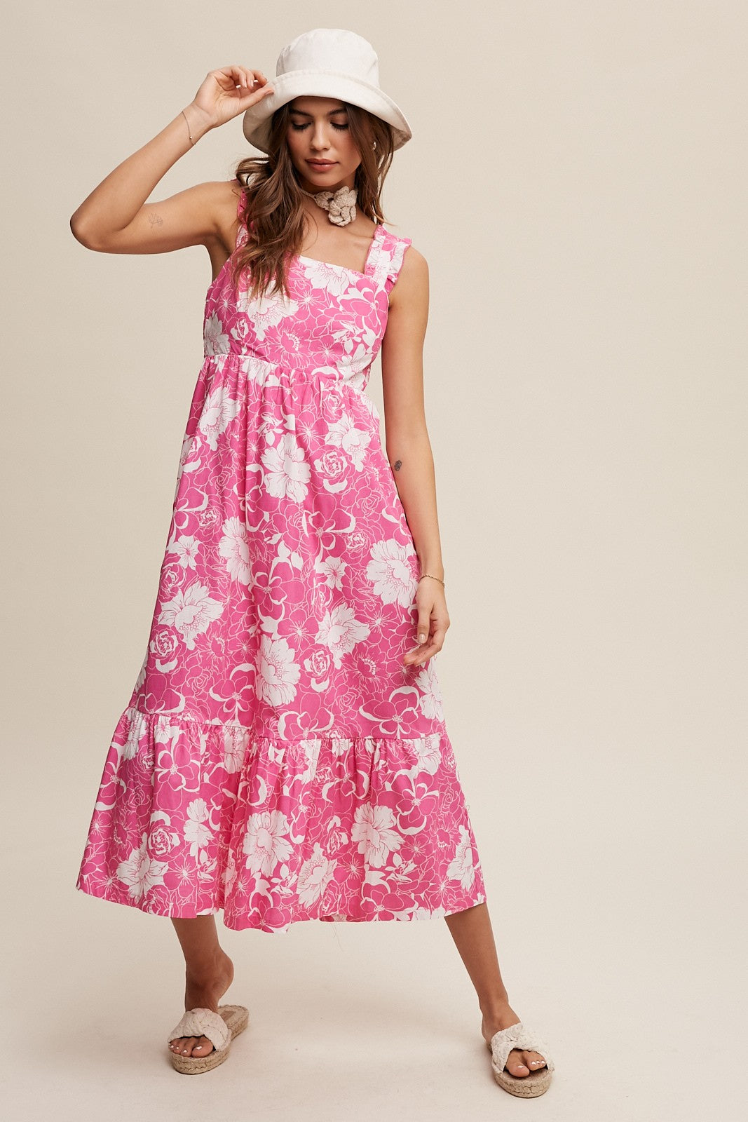 woman wearing a pink floral midi dress with tiered hem, accessorized with a white bucket hat and sandals