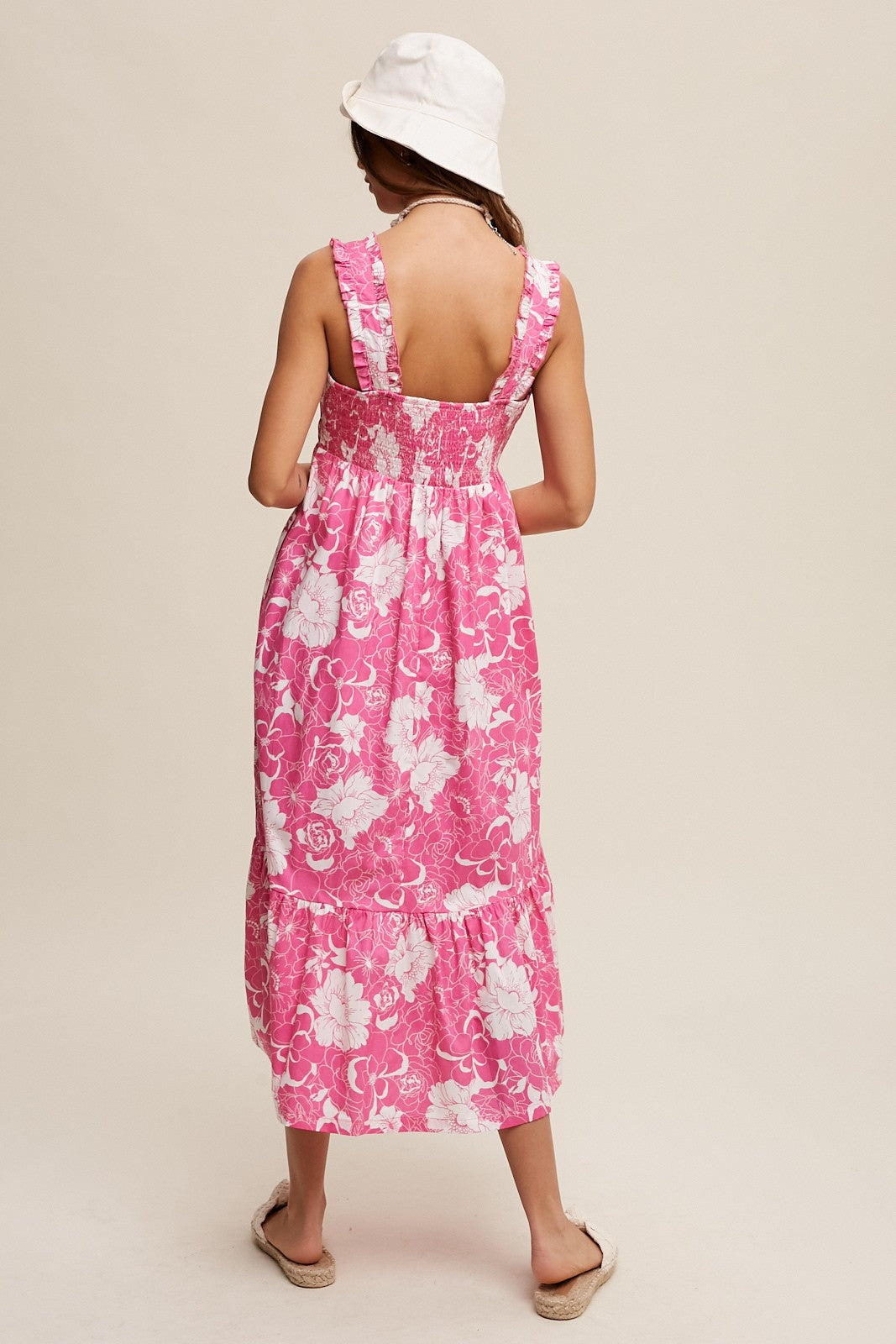woman wearing a pink floral maxi dress with a smocked back and tiered hem, styled with a white bucket hat