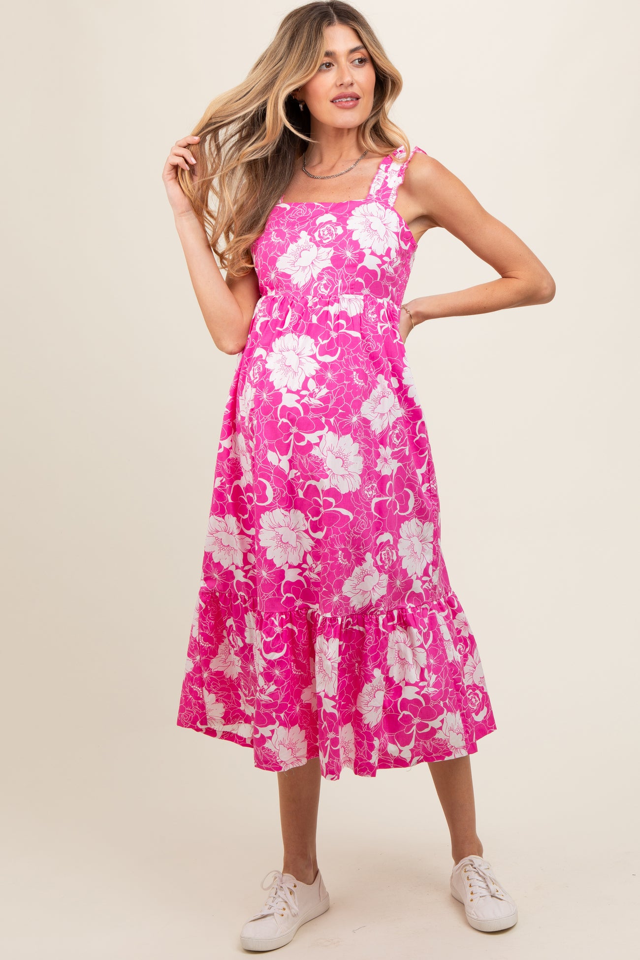 woman wearing a pink floral maternity dress with a flared hem and strappy design, showcasing her baby bump