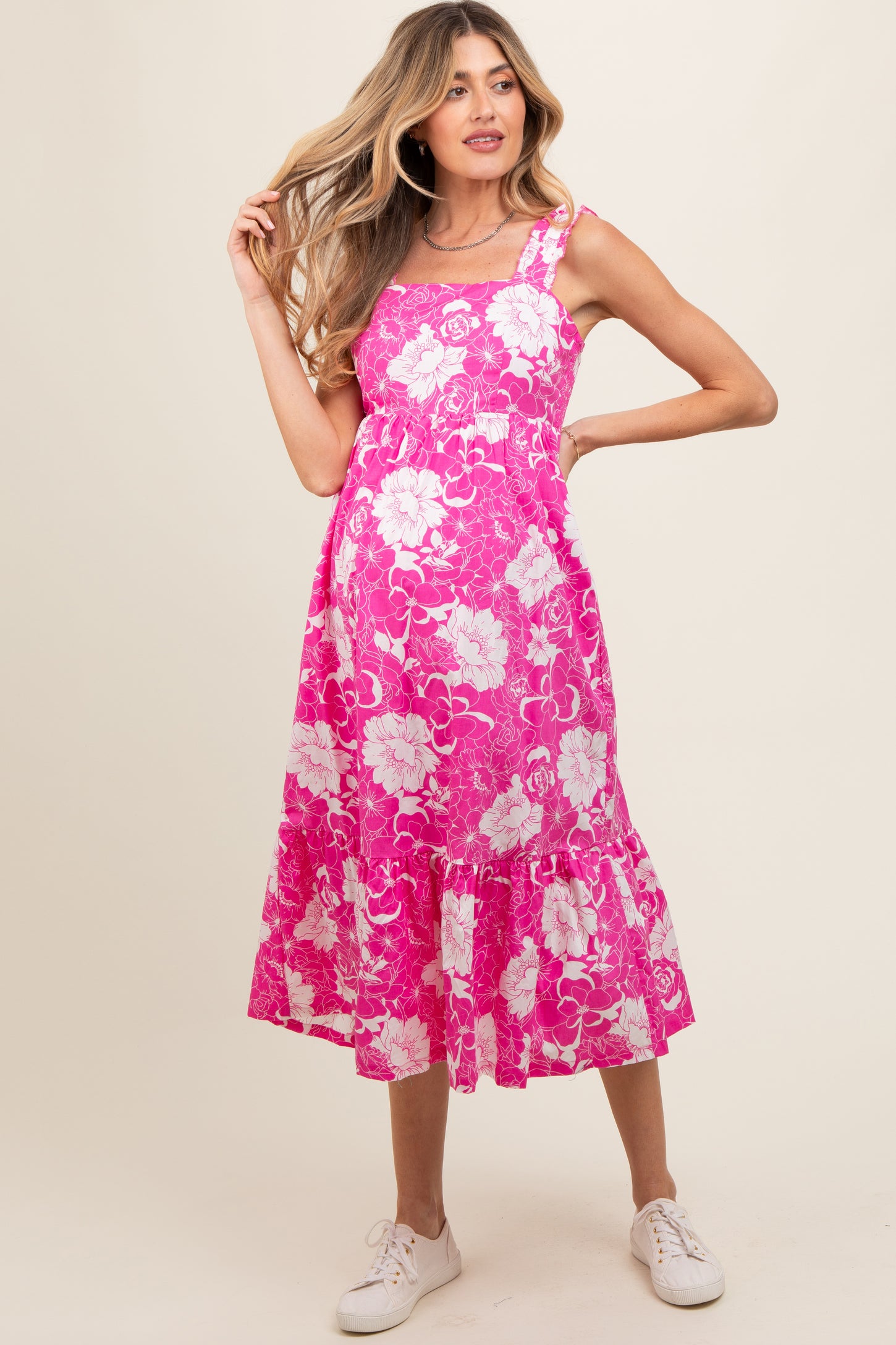 woman wearing a pink floral maternity dress with a flared hem and strappy design, showcasing her baby bump
