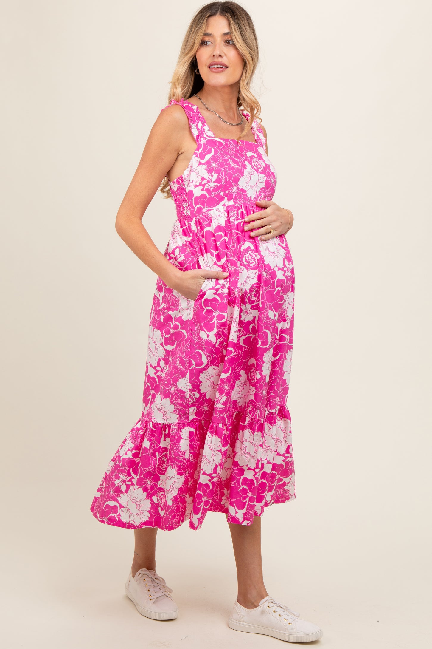 woman wearing a pink floral maternity dress with pockets and a visible baby bump