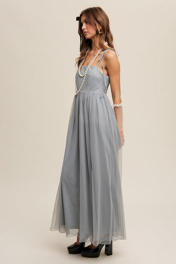 woman wearing a light gray maxi dress with thin straps and a flowing skirt, accessorized with pearls and gloves