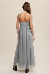woman wearing a light grey long tulle dress with adjustable spaghetti straps and a smocked bodice, seen from the back