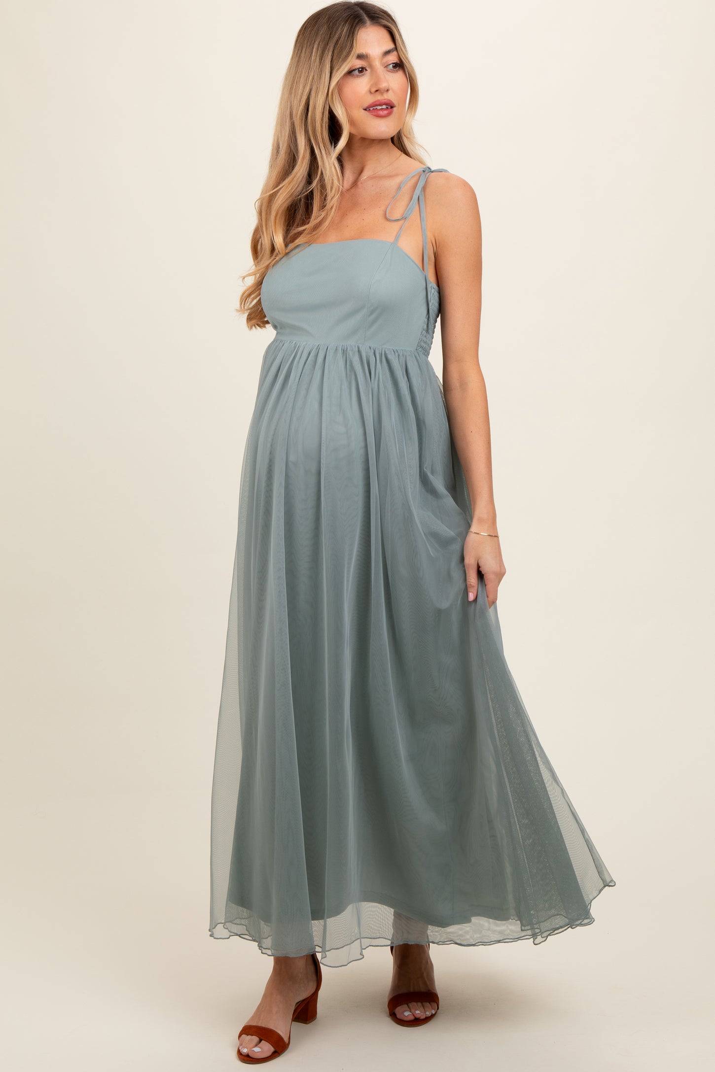 woman wearing a dusty blue maternity maxi dress with adjustable straps and a flowing skirt, showcasing her baby bump