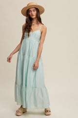 woman wearing a light green maxi dress with tiered ruffles and thin straps, styled with a straw hat and platform sandals