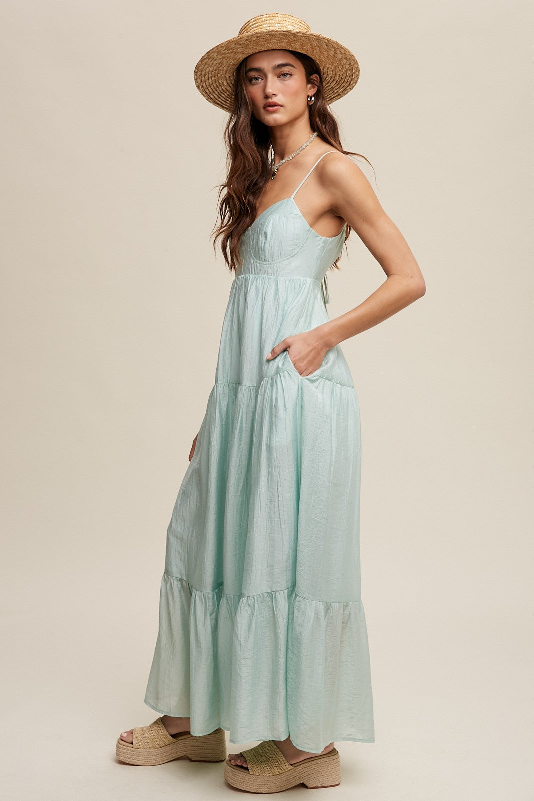 woman wearing a light green tiered maxi dress with pockets and a wide-brimmed straw hat