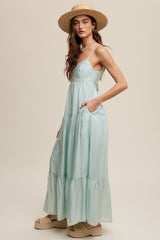 woman wearing a light green tiered maxi dress with pockets and a wide-brimmed straw hat