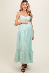 woman wearing a mint green maternity maxi dress with spaghetti straps and tiered detailing, holding her baby bump