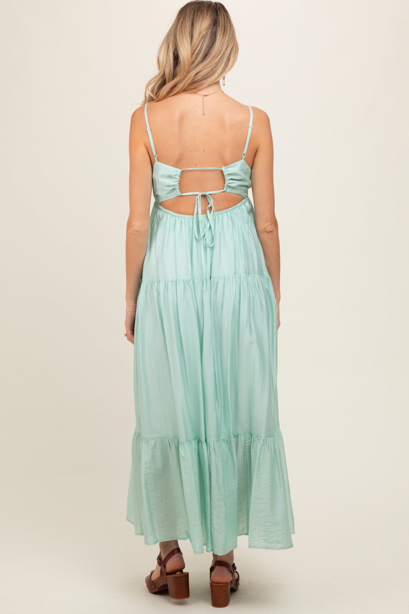 woman wearing a mint green backless maternity dress with adjustable spaghetti straps and a tiered skirt