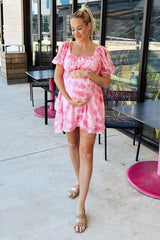 woman wearing a pink floral maternity dress and holding her baby bump while standing outside