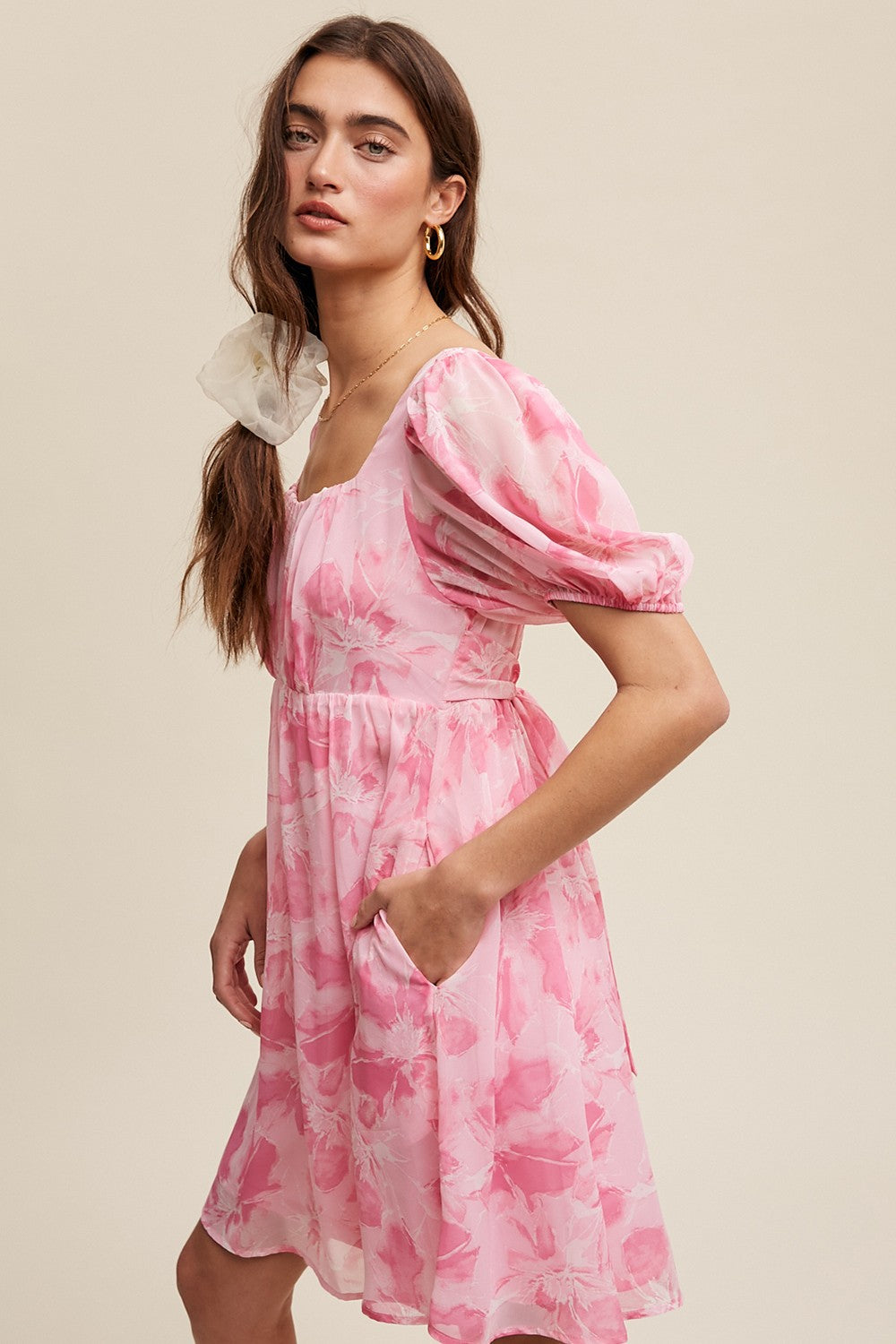 woman wearing a pink floral short puff sleeve dress with a square neckline and pockets