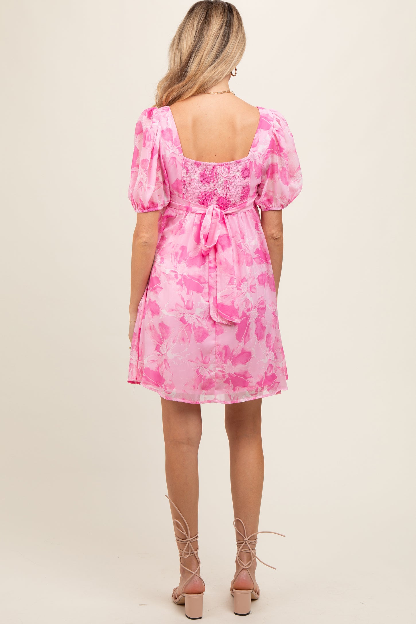 woman wearing a pink floral maternity dress with puff sleeves and a tie-back detail, showing her baby bump