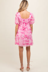 woman wearing a pink floral maternity dress with puff sleeves and a tie-back detail, showing her baby bump