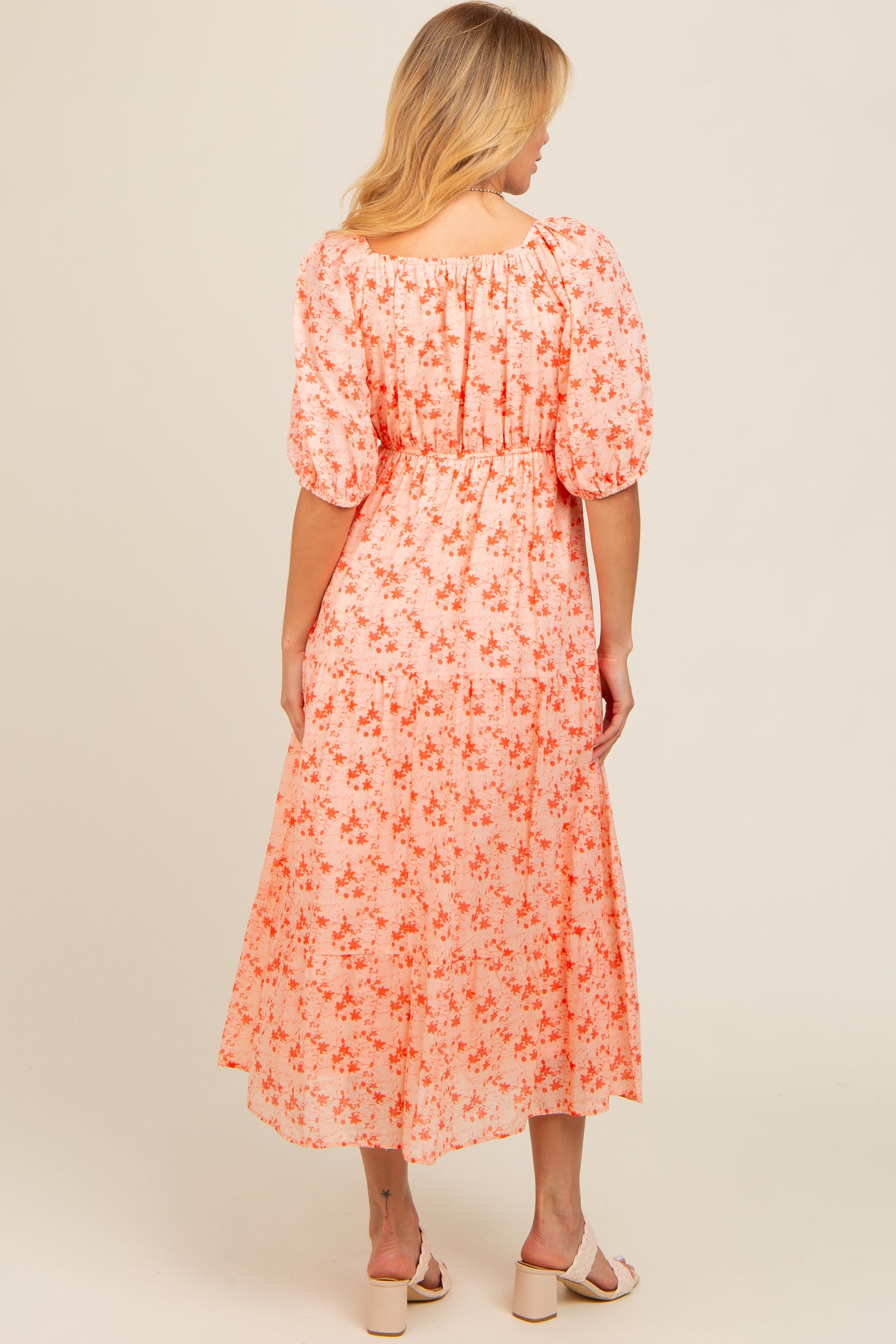 woman wearing a coral floral midi dress with puff sleeves and a smocked waist, shown from the back