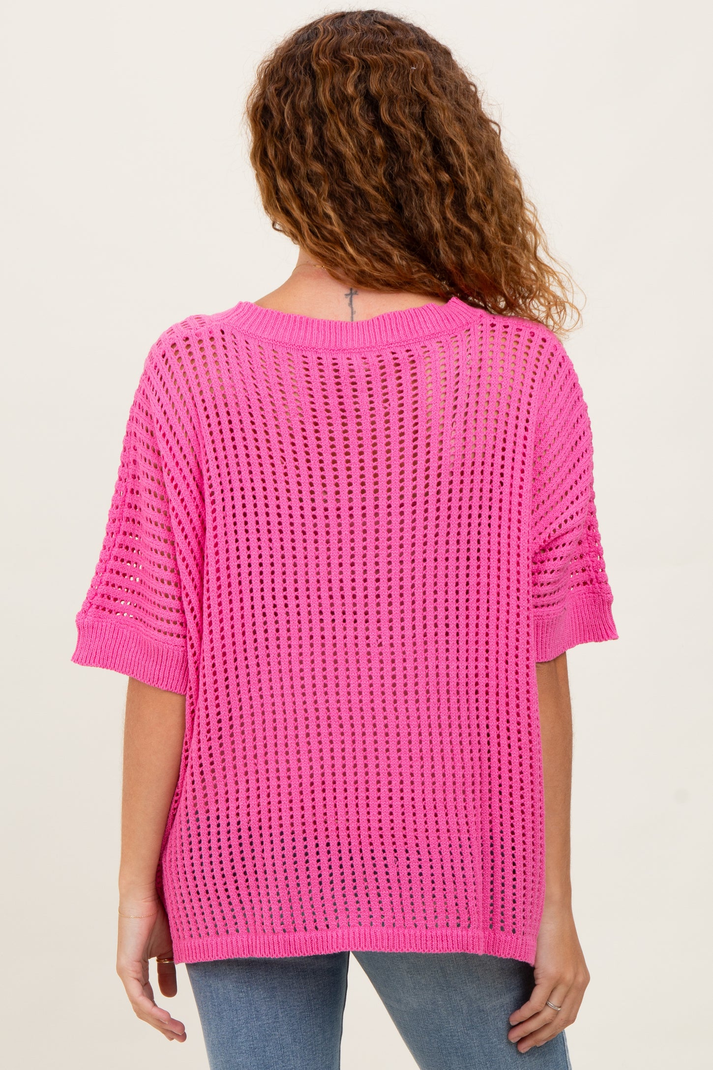 woman wearing an oversized bright pink open-knit sweater with short sleeves and a relaxed fit