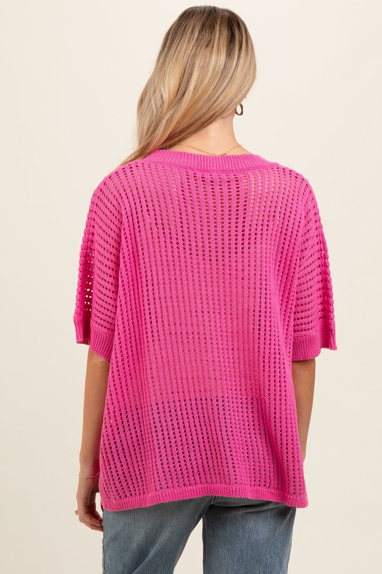 woman wearing a bright pink open knit maternity sweater with short sleeves and a relaxed fit from the back