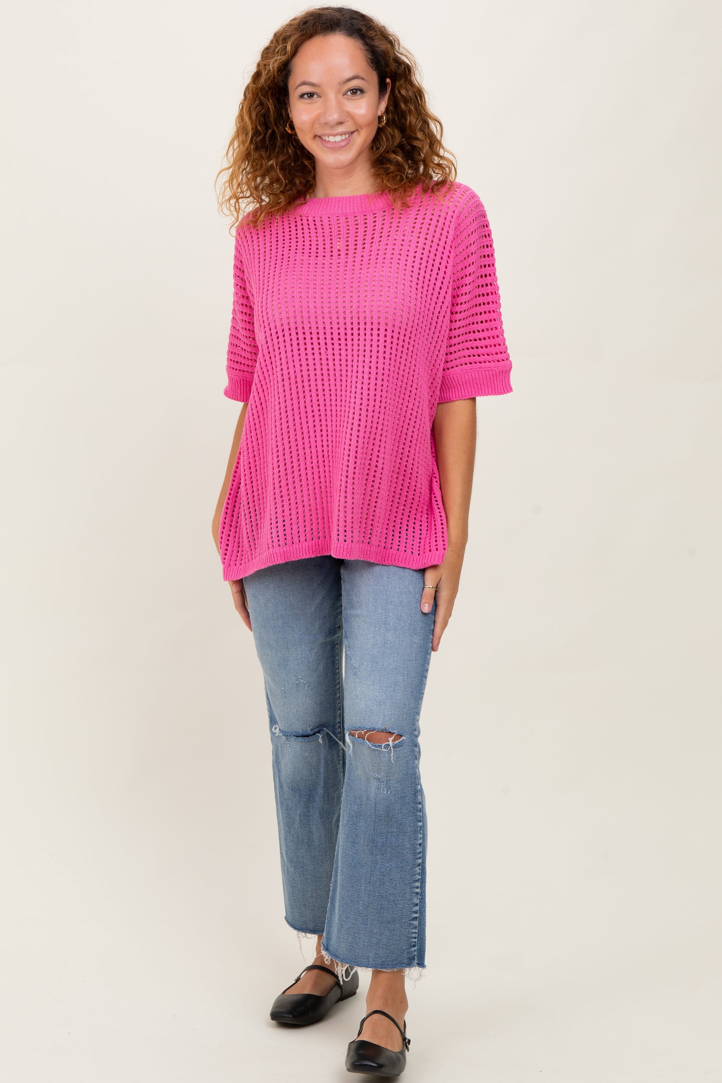woman wearing a bright pink oversized knit sweater and light wash ripped jeans