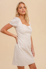 woman wearing a cream puff sleeve mini dress with a square neckline and textured pattern