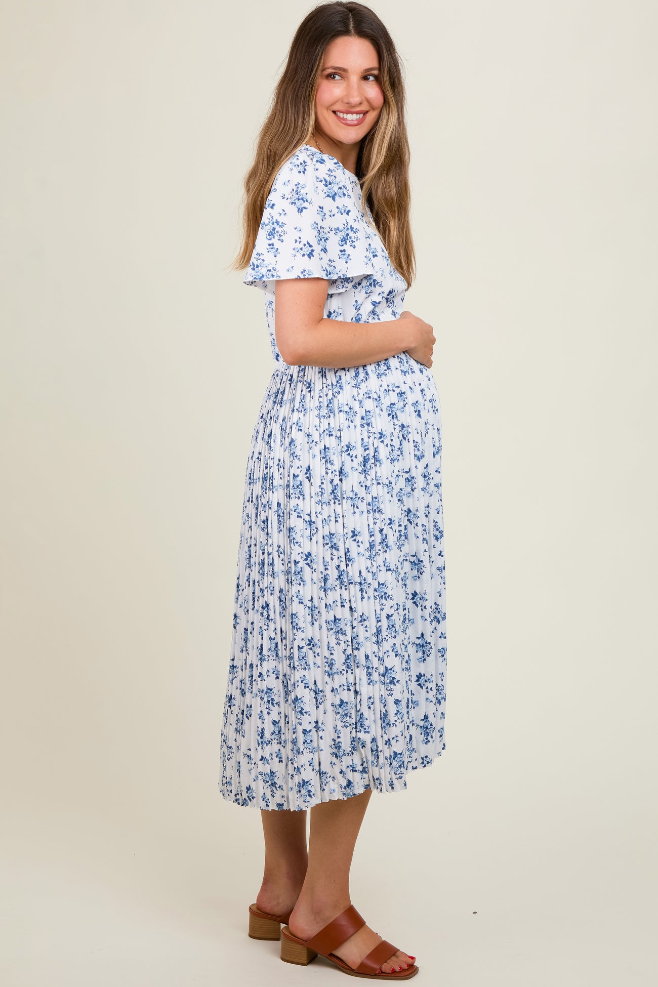 woman wearing a white floral maternity dress with short sleeves and a pleated skirt, cradling her baby bump