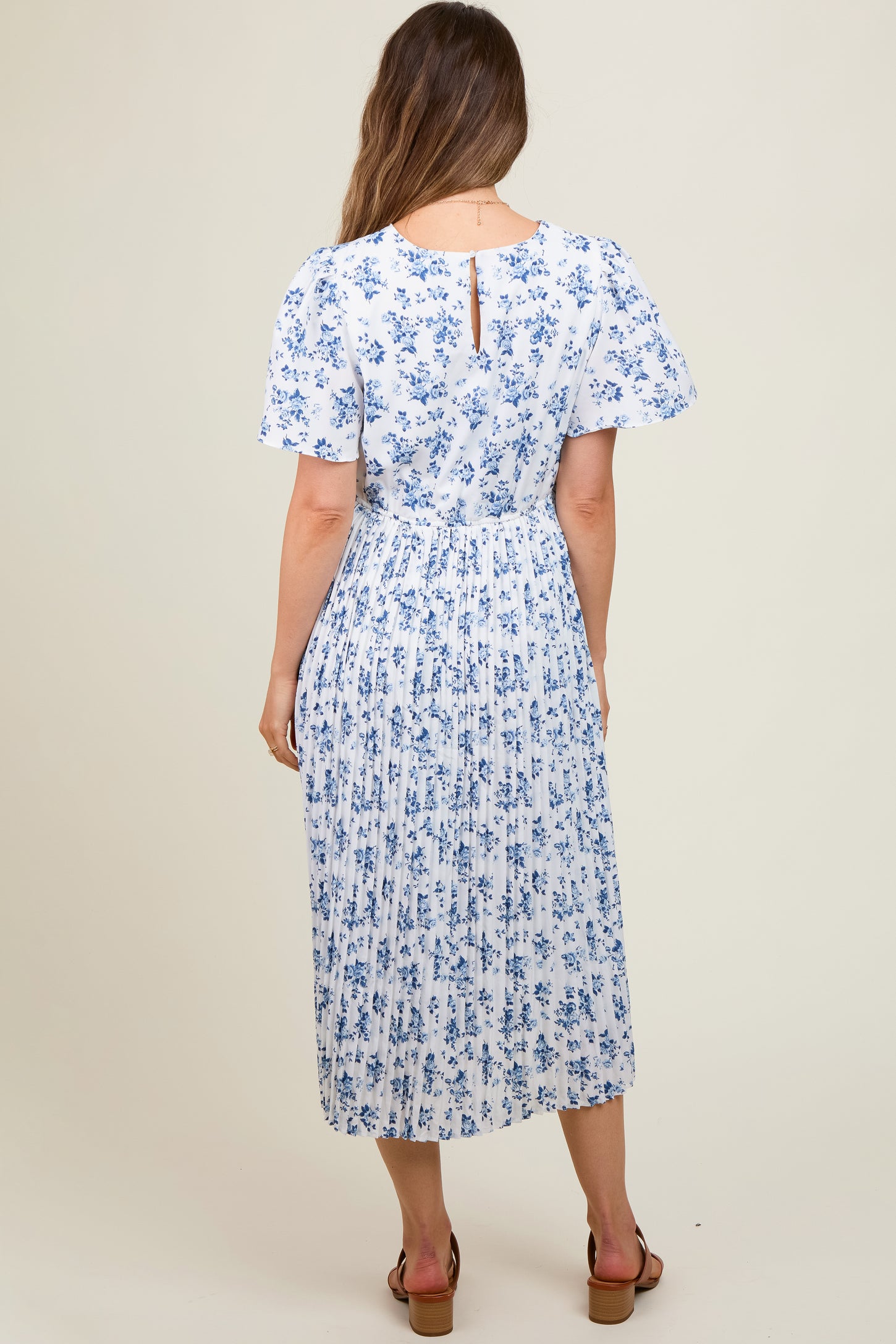 woman wearing a white floral print maternity dress with short sleeves and a pleated skirt, showing the back view