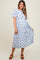 woman wearing a white floral maternity dress with pleats and flutter sleeves, standing and smiling