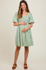 woman wearing a green floral maternity dress and holding her baby bump