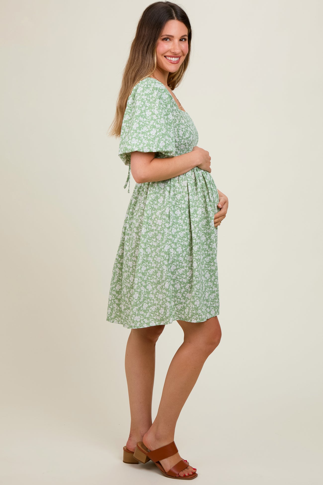 woman wearing a green floral maternity dress and holding her baby bump