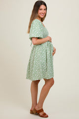 woman wearing a green floral maternity dress and holding her baby bump