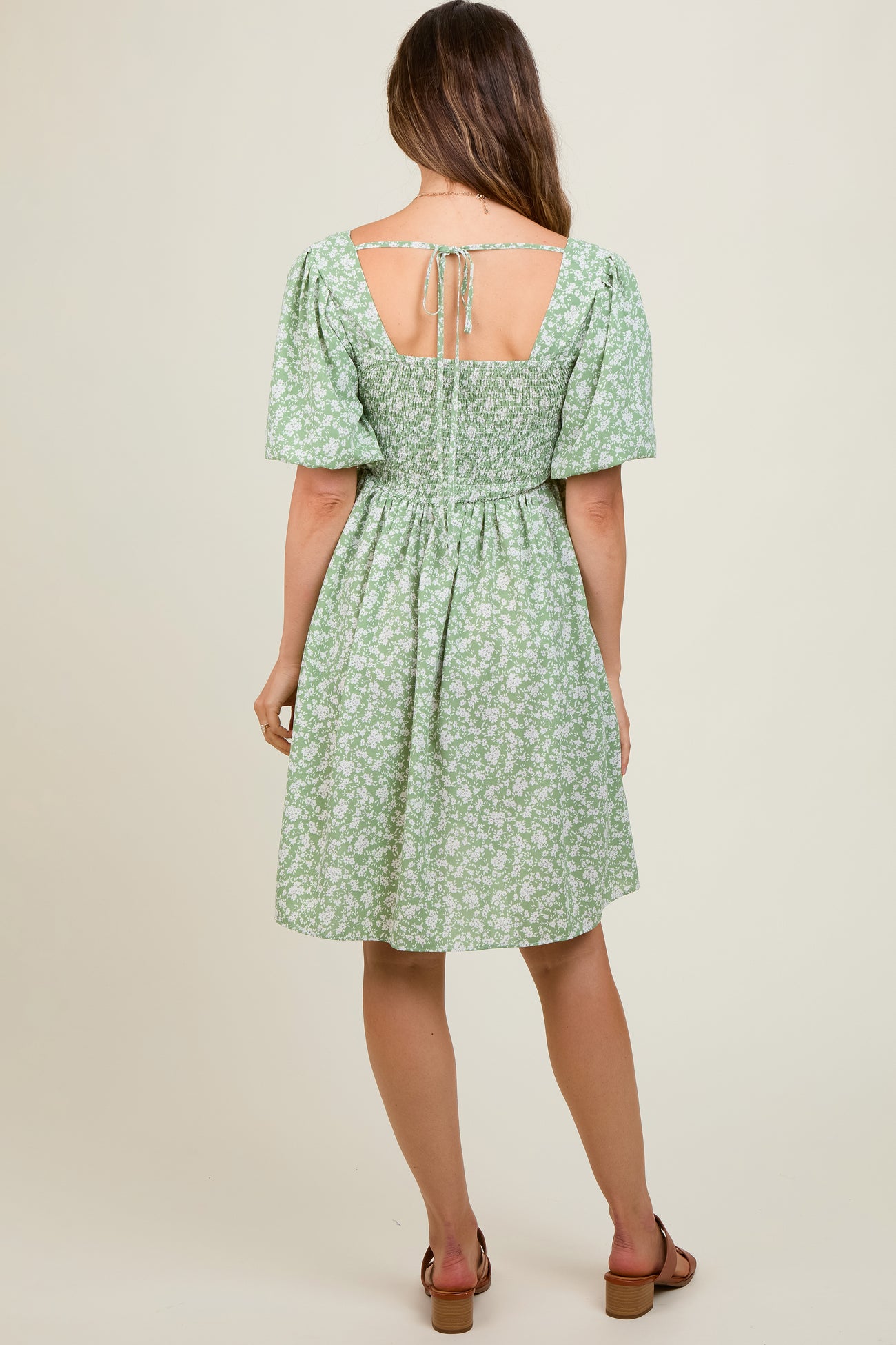 woman wearing a green floral short sleeve maternity dress with a tied back and fitted waistline