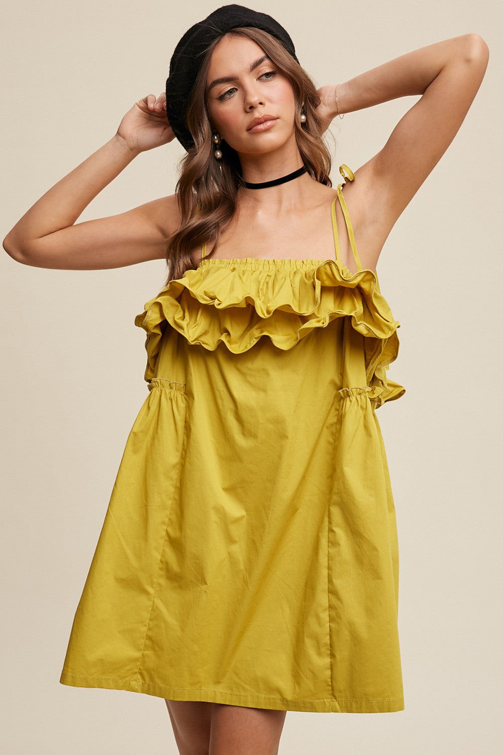 woman wearing a yellow ruffled mini dress with adjustable straps and a gathered waist