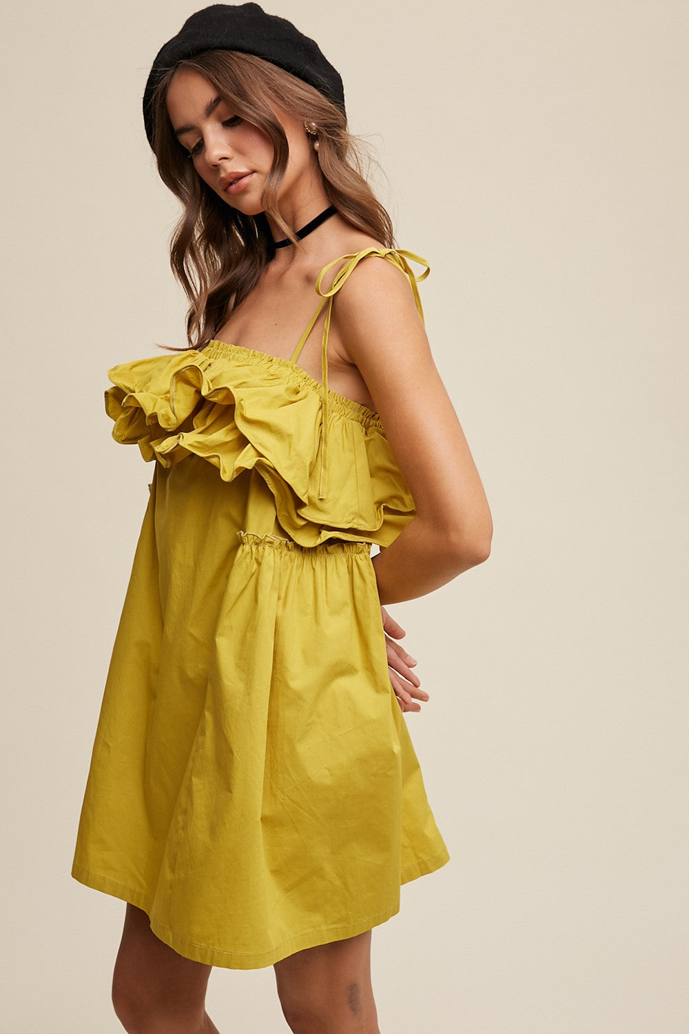woman wearing a yellow off-the-shoulder dress with ruffle details and adjustable straps, styled with a black beret and choker