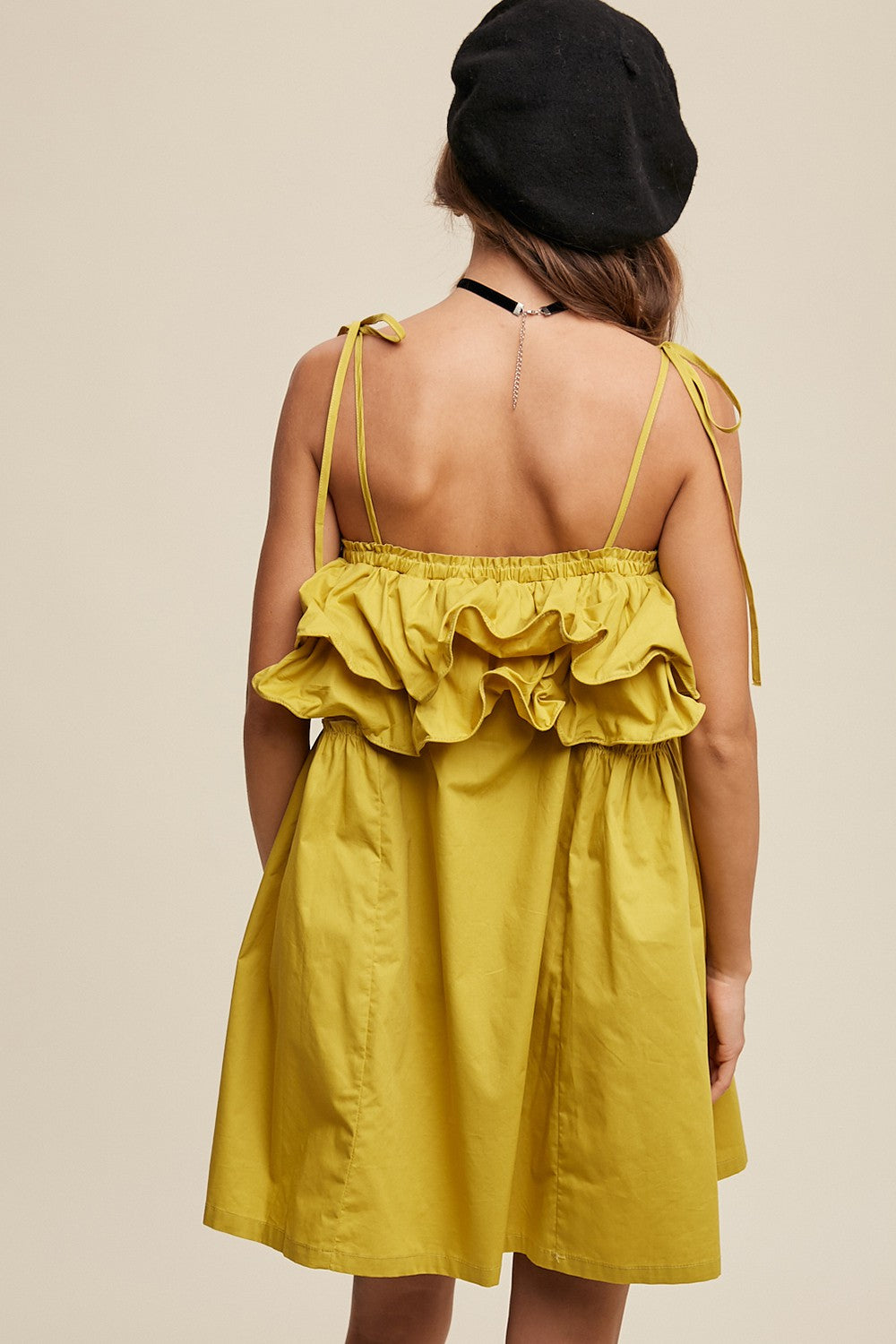 woman wearing a yellow sleeveless dress with a ruffled back and adjustable ties on the shoulders