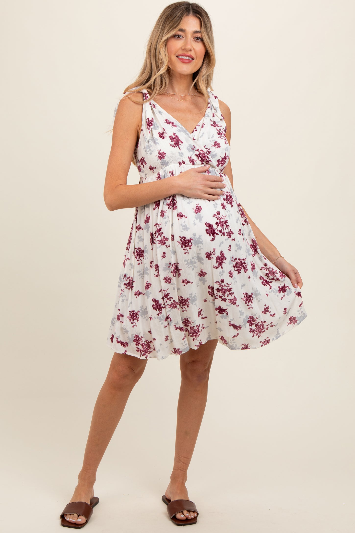 woman wearing a white floral maternity dress with a wrap design and adjustable straps, highlighting her baby bump