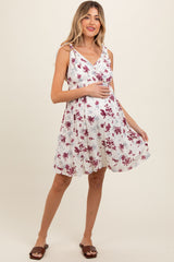 woman wearing a white floral maternity dress with a wrap design and adjustable straps, highlighting her baby bump