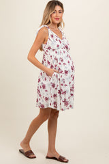 woman wearing a white floral maternity dress with tie straps and a visible baby bump, holding one pocket