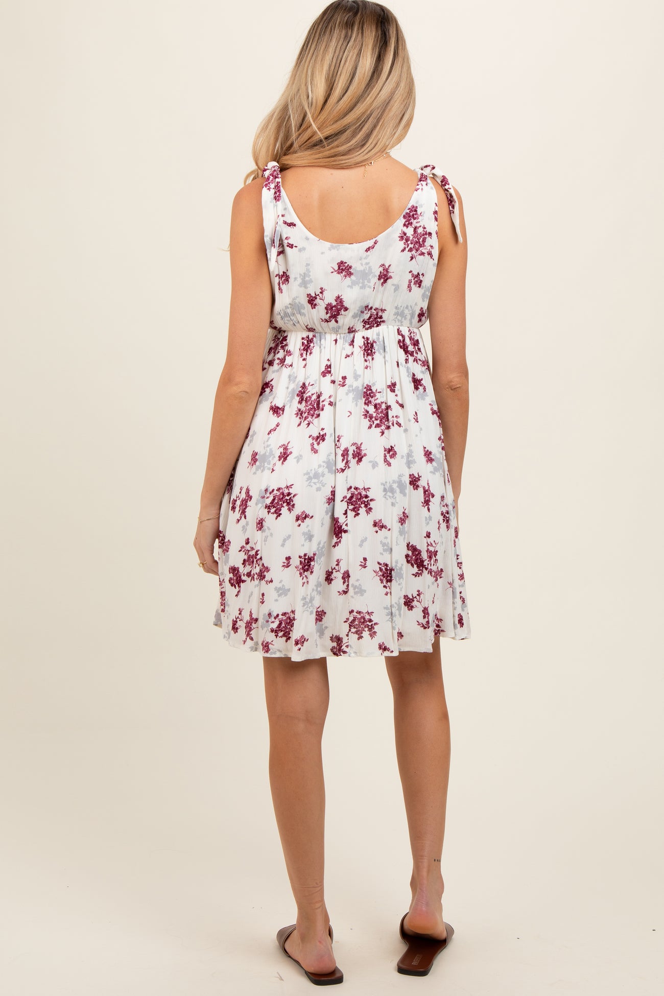 woman wearing a white floral maternity dress with adjustable tie straps and a loose fit, showing her baby bump from behind