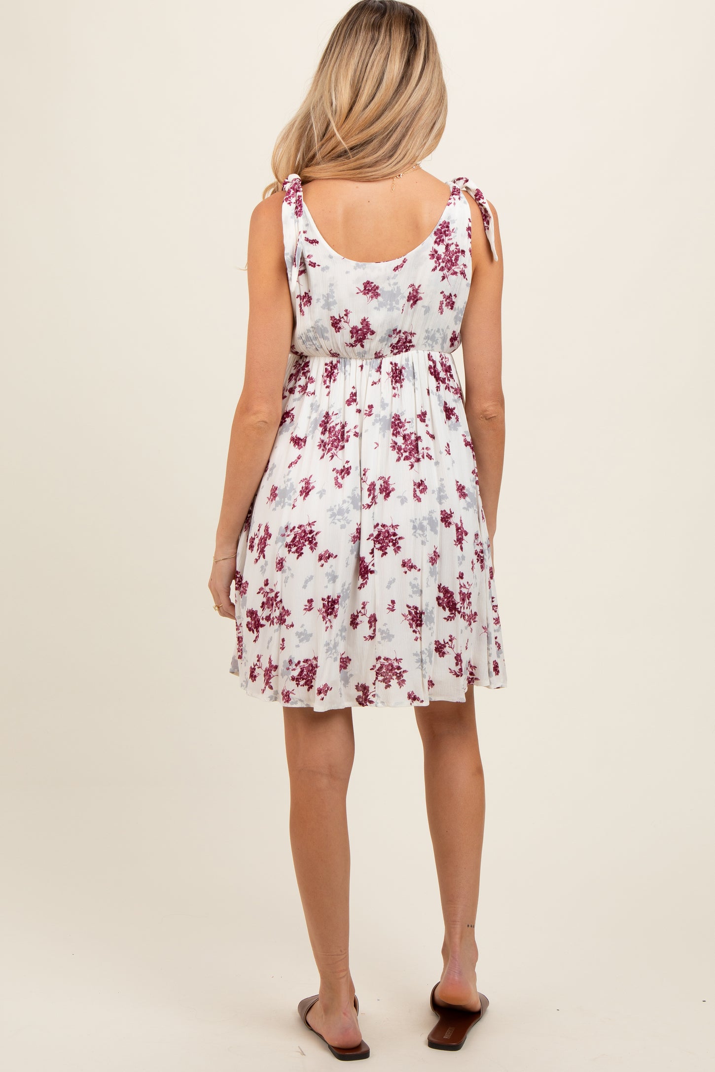 woman wearing a white floral maternity dress with adjustable tie straps and a loose fit, showing her baby bump from behind