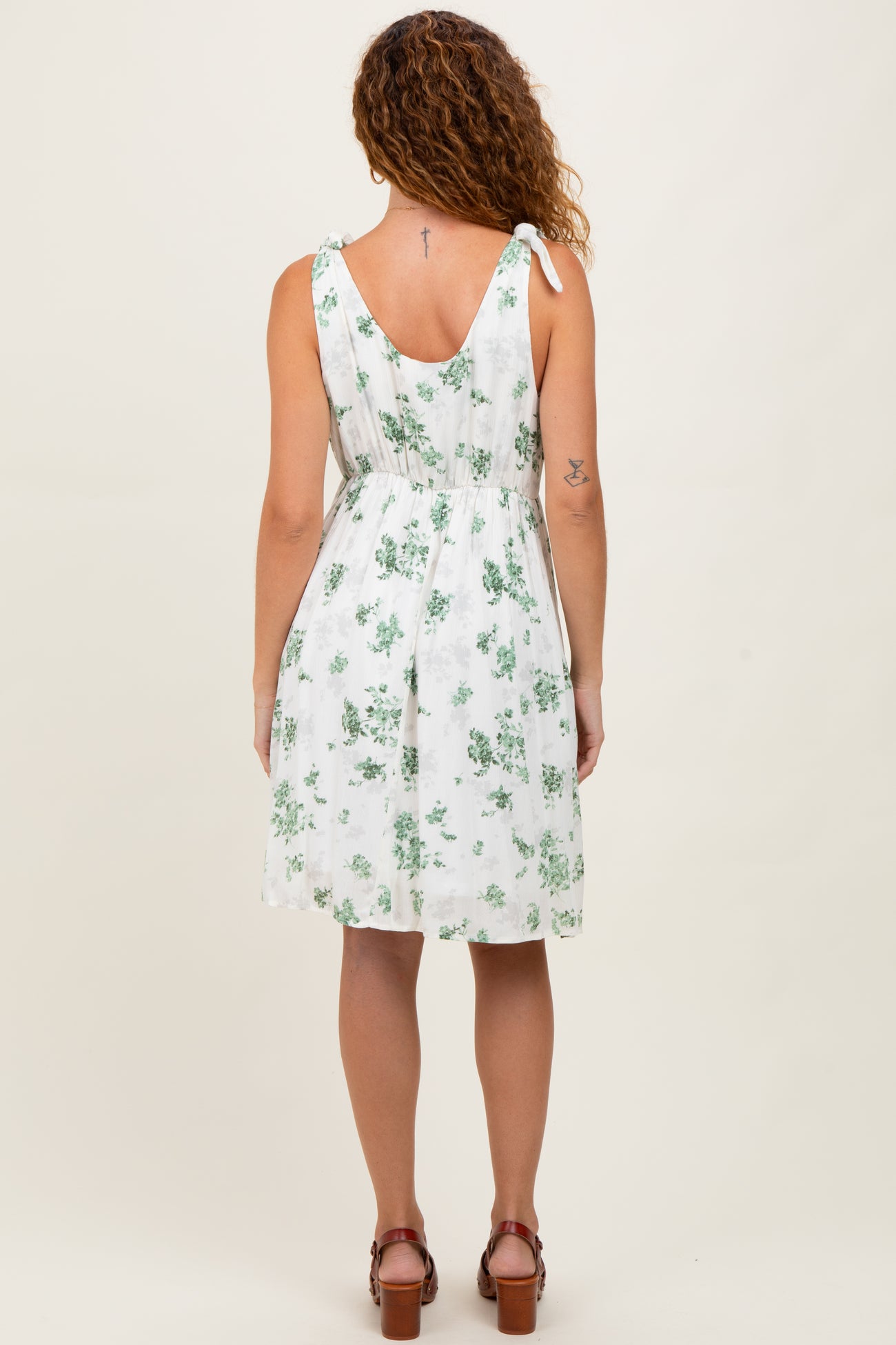 woman wearing a white floral sundress with ties at the shoulders and a cinched waist, viewed from the back