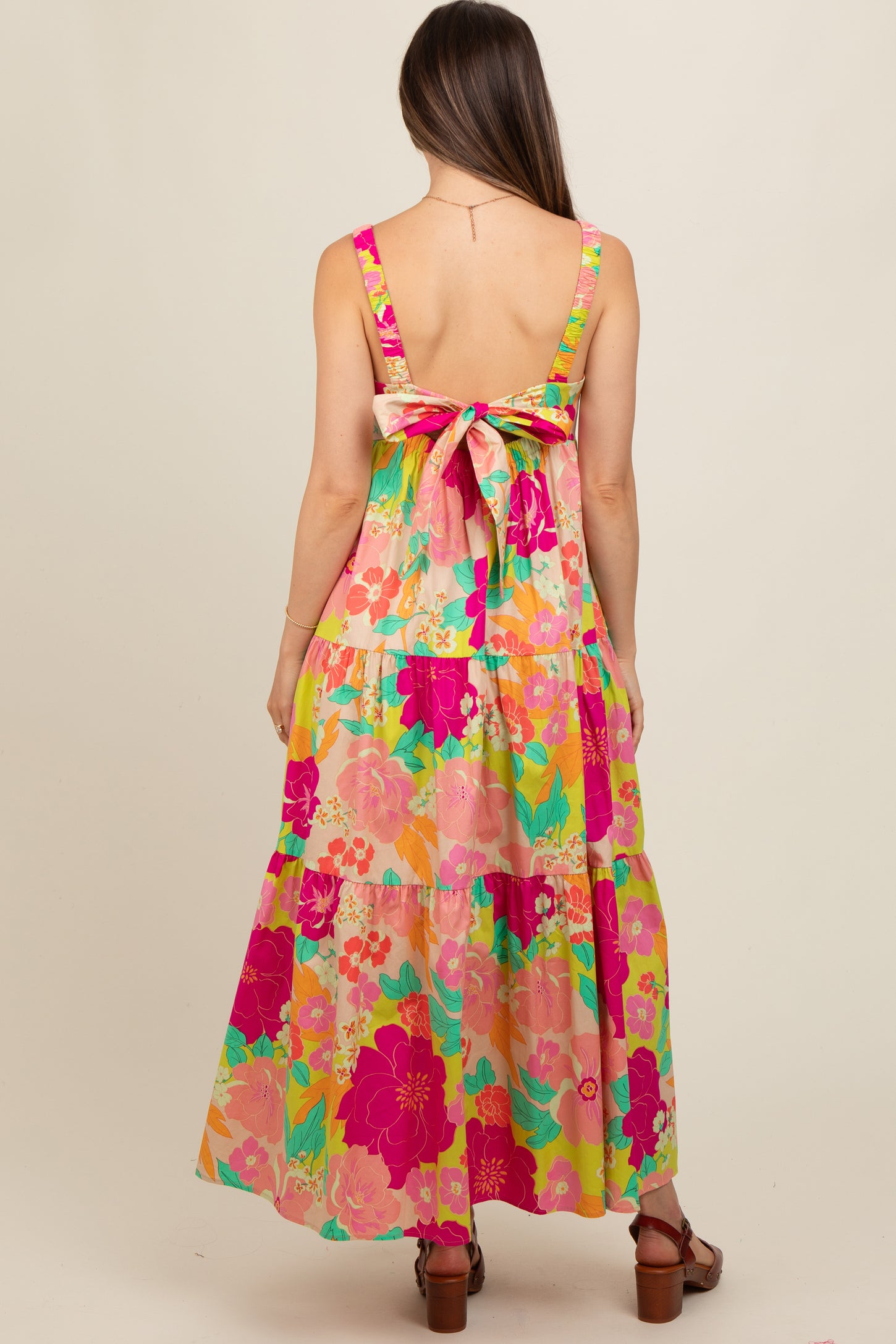 woman wearing a vibrant floral print maternity maxi dress with a bow detail on the back