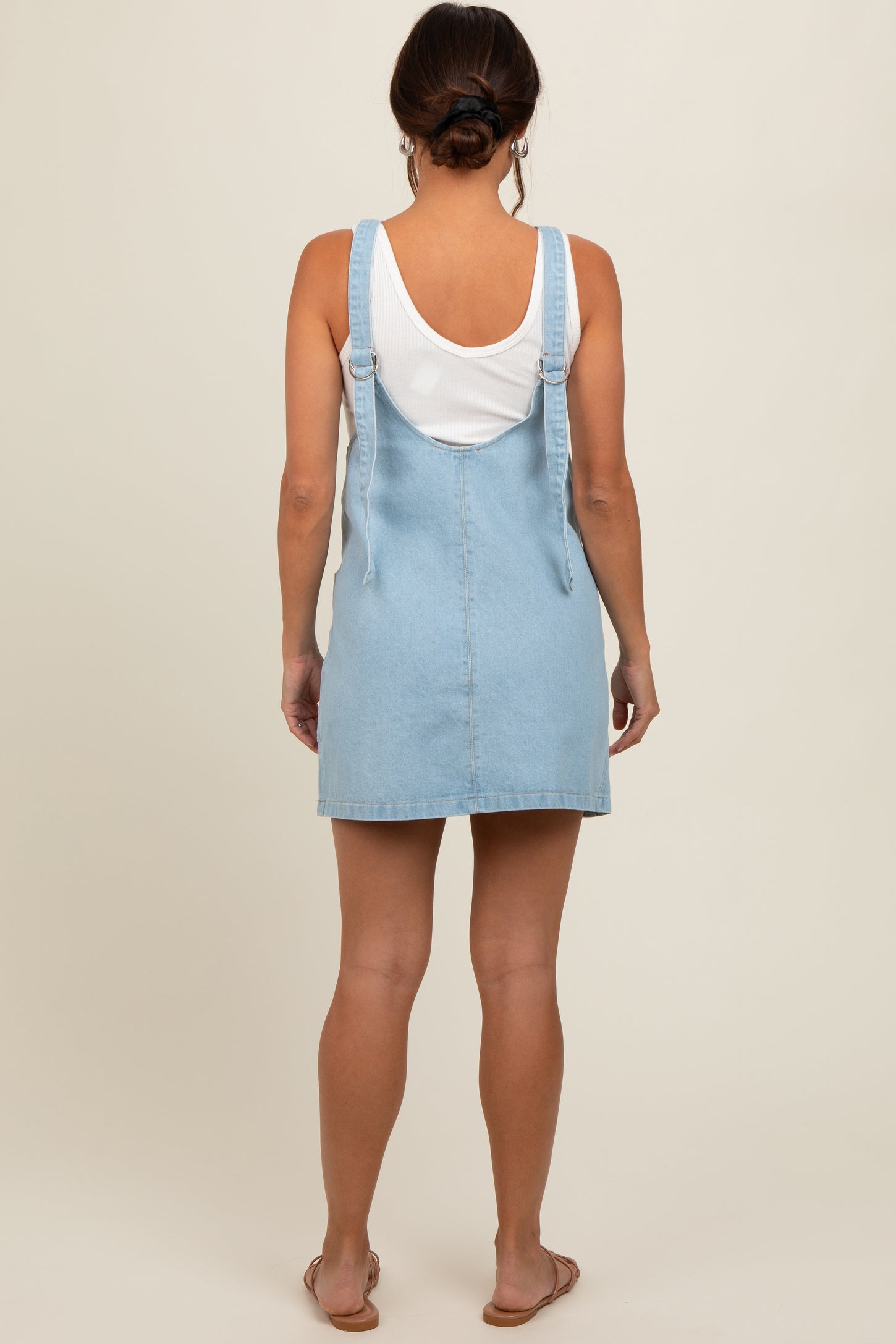 woman wearing a light blue denim maternity dress with adjustable straps, viewed from the back