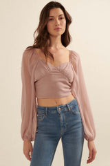 woman wearing a light pink cropped top with puff sleeves and ruched details, paired with blue jeans
